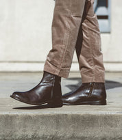 Wearing the Bed|Stü Kaldi brown leather ankle boots and beige corduroy pants, a person walks on a concrete sidewalk.