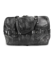 The Bed|Stü Keg is a black leather duffle travel bag featuring dual handles, front buckle accents, and a zippered top closure, expertly crafted from premium vegetable-tanned leather and showcased against a white background.