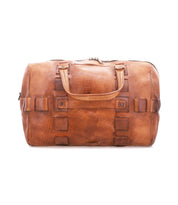 Introducing Keg by Bed|Stü—a timeless travel duffle crafted from vegetable tanned brown leather. This elegant bag features two sturdy handles, decorative stitching with rectangular accents, and a secure zipper closure, all set against a white background—the perfect companion for any journey.