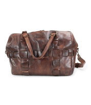 The Bed|Stü Keg duffle bag, crafted from premium vegetable tanned brown leather with woven square accents, features dual handles and an adjustable shoulder strap, shown against a white background.