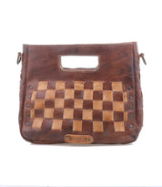 The Keiki crossbody bag by Bed|Stü showcases a brown leather checkerboard design with woven light and dark squares, a rectangular handle cutout, and metal rivet accents on the front. It features a zip-top closure and comes with an adjustable strap for added convenience.