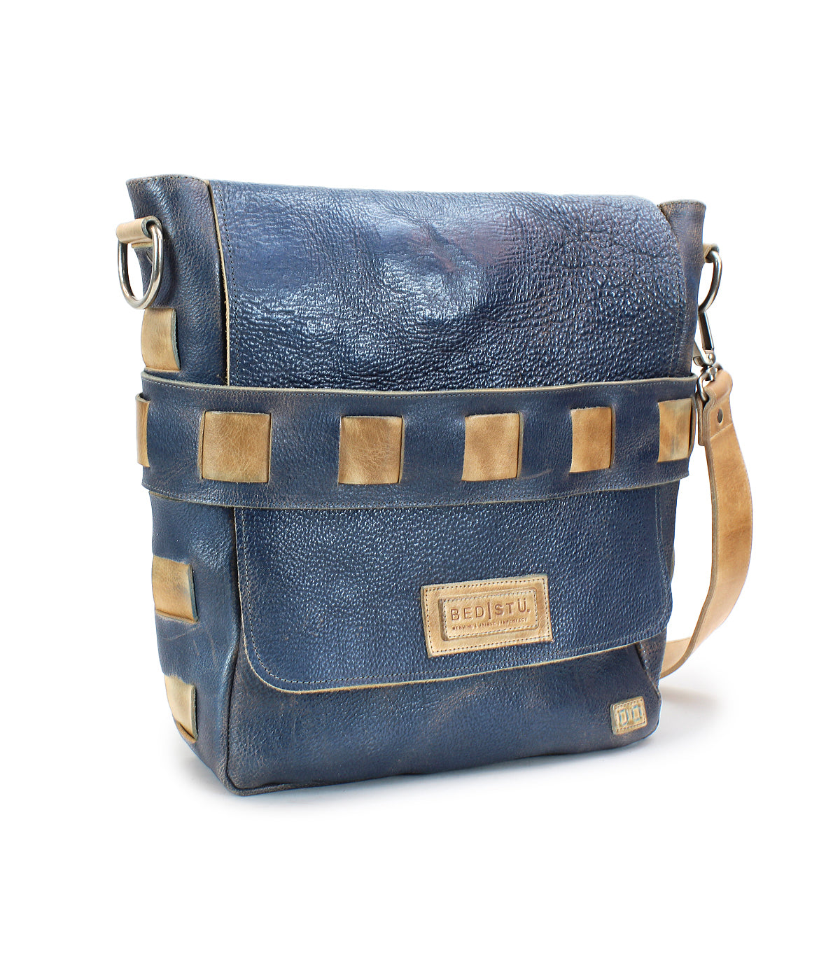 The Kure messenger bag by Bed|Stü is crafted from blue leather with tan square accents, featuring a vegetable-tanned leather shoulder strap and a front flap adorned with a stitched Bed|Stü label. The bag is displayed on a white background.