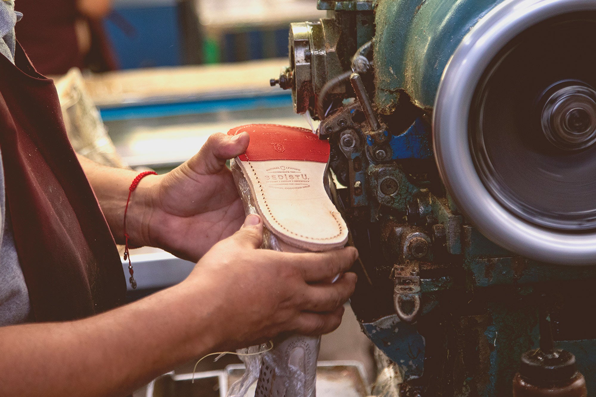 Craftsperson stitching a BED|STU leather shoe sole with an industrial machine in a workshop.