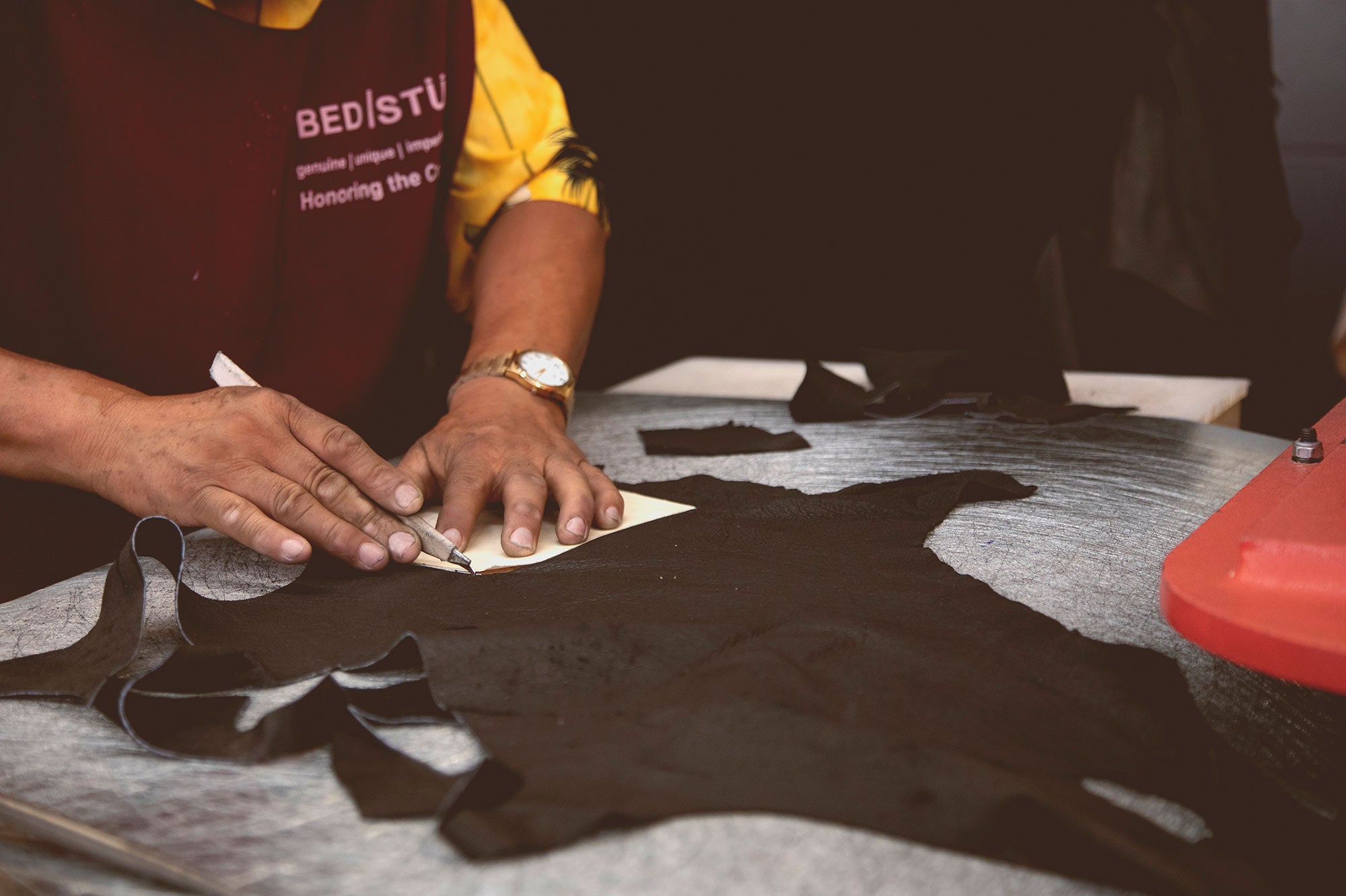 Craftsperson cutting black leather around a pattern template on a worktable.