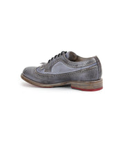 A single gray leather Bed|Stü Lita K wingtip oxford shoe with brogue details, a brown stacked sole, and a red accent on the heel, viewed from the side.