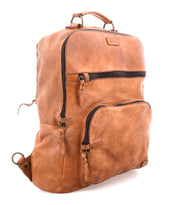The Bed|Stü Lafe brown leather backpack features two zippered front pockets, a top handle, and metal hardware, designed as a 17-inch laptop bag that combines style and practicality—shown here on a white background.
