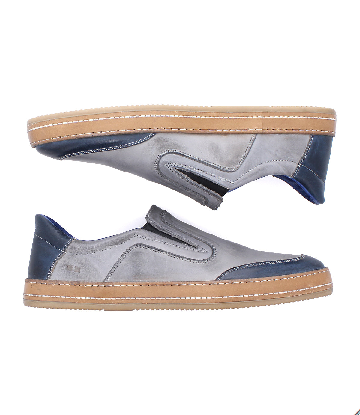 Introducing the Bed|Stü Lanius: a pair of gray slip-on sneakers featuring tan soles, navy blue accents on the heel and toe, and visible stitching. These shoes showcase a timeless silhouette enhanced with modern color blocking, beautifully displayed side by side on a white background.