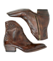 The Bed|Stü Laredoa boots are a pair of brown leather ankle boots with side zippers, decorative stitching, and low stacked heels; these feminine cowboy boots showcase a subtle Western flair and are displayed on a white background.