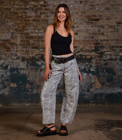 A woman stands indoors against a textured brick wall, wearing a black tank top, snakeskin print pants with a wide belt, and Bed|Stü's Library black platform sandals that channel true ‘90s style.