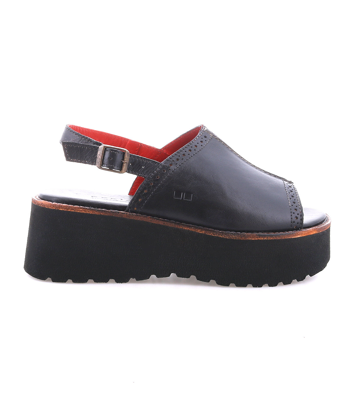 The Bed|Stü Library is a black platform sandal featuring an open toe, adjustable ankle strap, and a thick black sole. Made with leather uppers highlighted by subtle stitching details, this sandal embodies the essence of ‘90s retro style. Shown against a white background.
