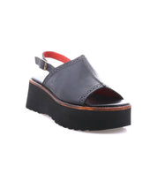 The Bed|Stü Library is a black leather platform sandal featuring an open toe, a back strap with buckle, and a thick ridged sole—displayed on a white background, this retro design captures the bold spirit of ‘90s style.