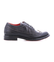 The Bed|Stü Lita K II is a single black leather dress shoe with classic brogue detailing and a wingtip toe, featuring decorative perforations, lace-up closure, and a low heel, shown in profile against a white background.
