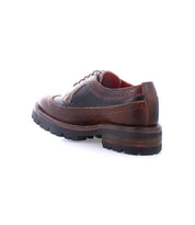 The Bed|Stü Lita K III is a brown leather brogue dress shoe featuring a thick, rugged sole and vintage-inspired detailing, shown from the back left side on a white background.