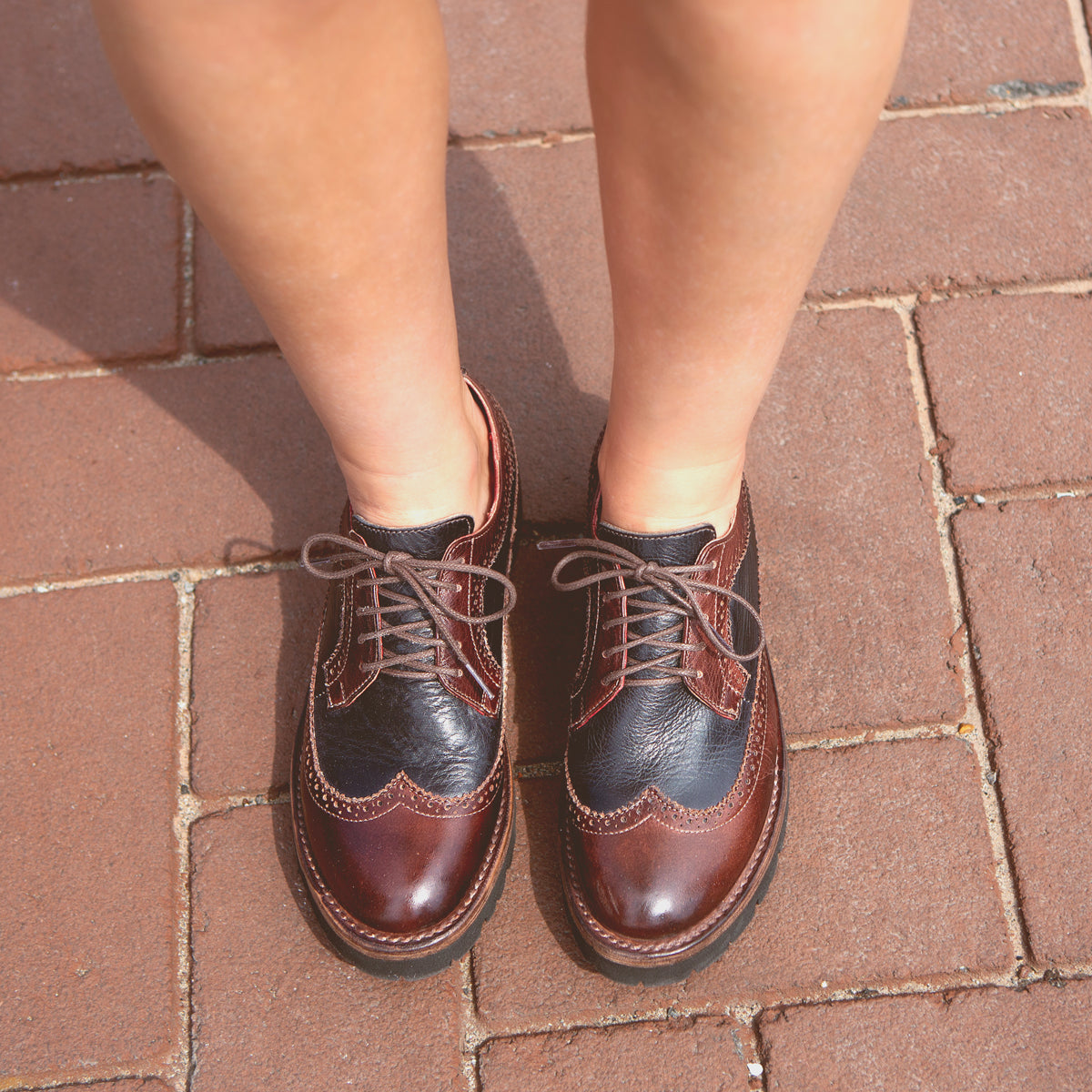 Person standing on a brick sidewalk wearing the Bed|Stü Lita K III vintage-inspired brown and black leather oxford shoes with laces, viewed from above.