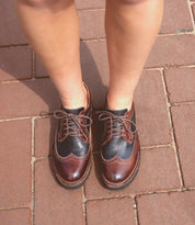 Person standing on a brick sidewalk wearing the Bed|Stü Lita K III vintage-inspired brown and black leather oxford shoes with laces, viewed from above.