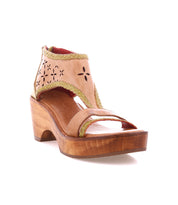 The Locket by Bed|Stü is a tan leather open-toe sandal, showcasing laser-cut floral detailing and decorative cutouts, with a sculpted wooden platform heel, ankle strap, and distinctive green stitching—all presented against a white background.