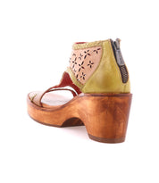 The Bed|Stü Locket sandal is displayed from a rear angle, showcasing its sculpted wooden heel, laser-cut floral leather design, back zipper, and green leather accents.