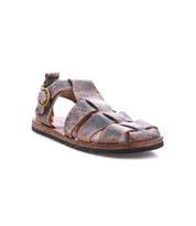 The Bed|Stü Lone sandal is crafted from brown distressed leather and features a closed toe, open sides, an antique brass buckle strap, and a flat sole with a contoured footbed; photographed on a white background.