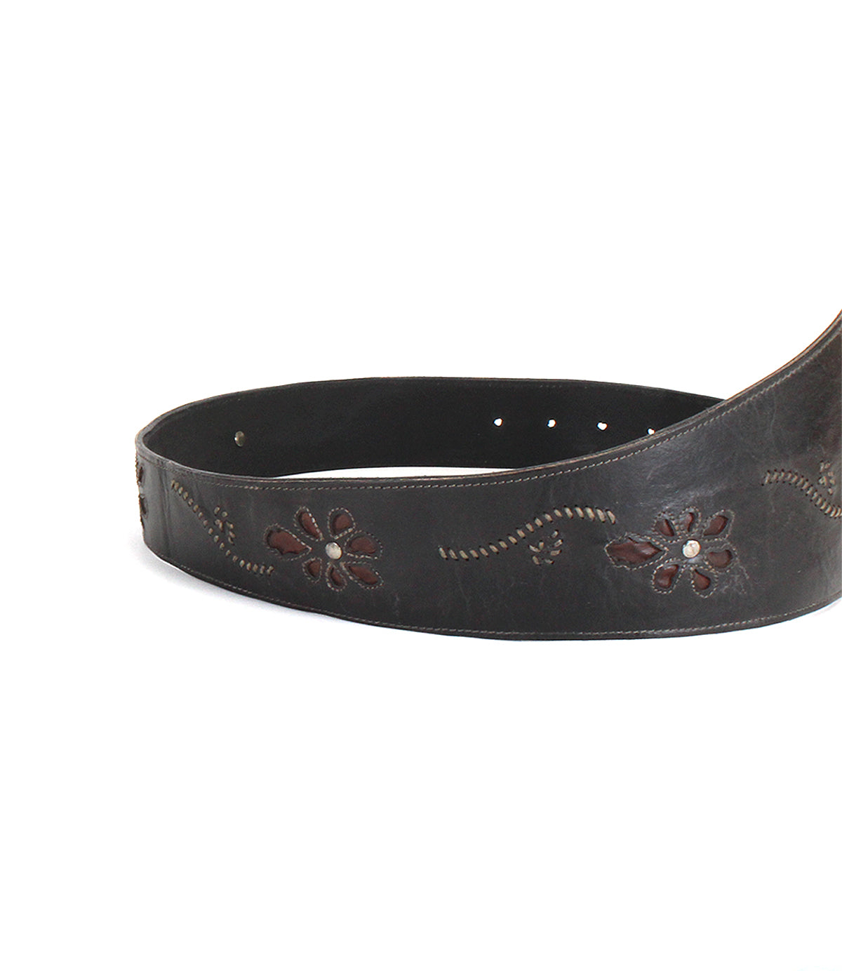 The Bed|Stü Lucen belt, featuring dark leather with boho-chic floral patterns and decorative stitching, is partially coiled on a white background and serves as a striking accessory that infuses any outfit with personality.