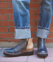 A person stands on a paved surface in front of a brick wall, wearing cuffed blue jeans and the Bed|Stü Lydyi leather ankle boots, which feature a platform outsole and cushioned insole.