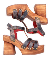 A pair of Bed|Stü Lyxon vintage-style black leather sandals featuring open toes, wooden chunky heels, brass rivets, a red interior lining, and buckle straps.