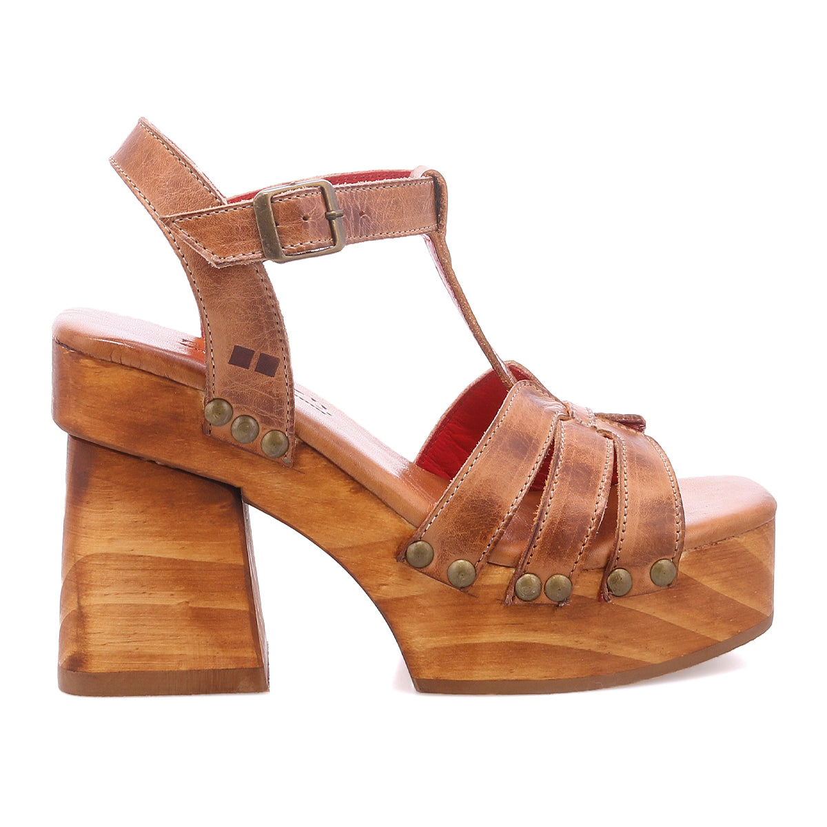 The Bed|Stü Lyxon is a brown leather platform sandal featuring a chunky wooden platform heel, metal rivet accents, and a buckle ankle strap. Styled in an open-toe silhouette, it is shown in a left-facing side profile against a white background.