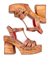 The Lyxon sandals by Bed|Stü are brown leather platform sandals featuring a T-strap design, wooden chunky heels, brass rivet detailing, and an open-toe silhouette, shown from the side.