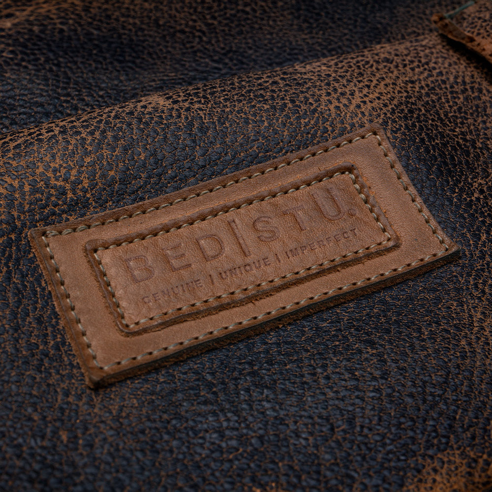 Close-up of a brown leather patch embossed with “BED|STU” on textured dark leather.