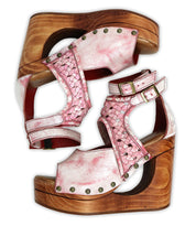 A pair of Bed|Stü Magic sandals in pink, displayed side by side on a white background, features a handwoven leather upper with a peep-toe design, sculpted wooden wedge heels, metal studs, and ankle straps.