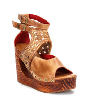 The Bed|Stü Magic sandal is a brown leather wedge featuring a handwoven leather upper with woven straps, metal buckles, and stud accents, all set on a sculpted wooden wedge platform heel and displayed against a white background.