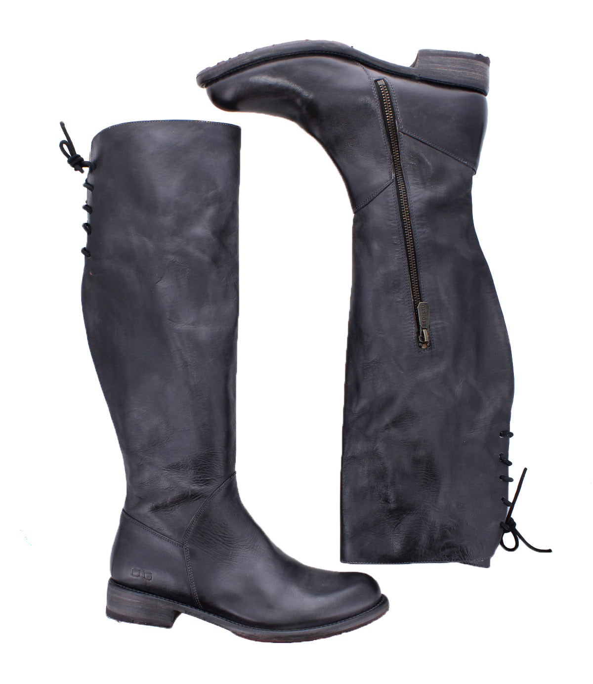 Two tall black leather "Manchester" boots by Bed|Stü, one standing upright and the other lying on its side, showcase distinctive zipper and lace-up detailing at the back. This modern classic style features a comfortable flat heel, combining timeless design with everyday wearability.