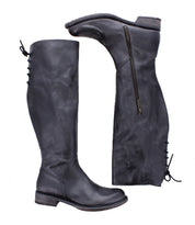 Two tall black leather "Manchester" boots by Bed|Stü, one standing upright and the other lying on its side, showcase distinctive zipper and lace-up detailing at the back. This modern classic style features a comfortable flat heel, combining timeless design with everyday wearability.
