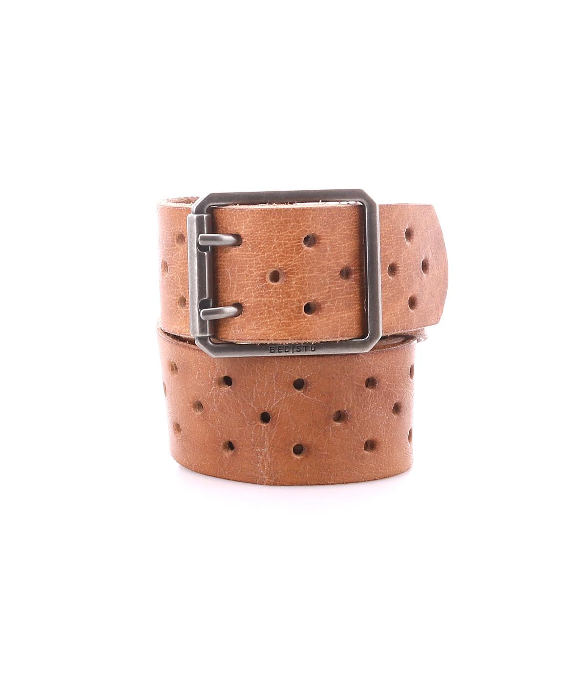 The Bed|Stü Mccoy is a brown leather strap belt featuring multiple round holes and a durable metal buckle, shown coiled on a white background for adjustable, customizable fit.