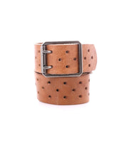 The Bed|Stü Mccoy is a brown leather strap belt featuring multiple round holes and a durable metal buckle, shown coiled on a white background for adjustable, customizable fit.