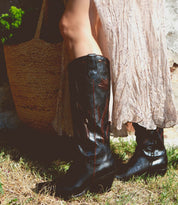 Wearing the Meadow light, flowing skirt and Bed|Stü handcrafted Italian boots, the person stands on grass beside a woven straw bag.
