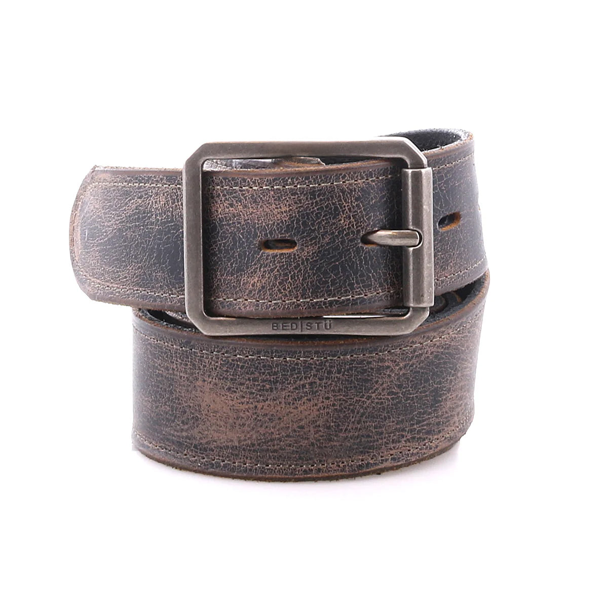 The Bed|Stü Meander is a rolled-up, distressed leather belt featuring an antique metal buckle and a rugged look, displayed on a white background.