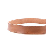 The Bed|Stü Meander is a single tan distressed leather belt, designed in a circular shape and featuring an antique metal buckle, displayed against a white background.