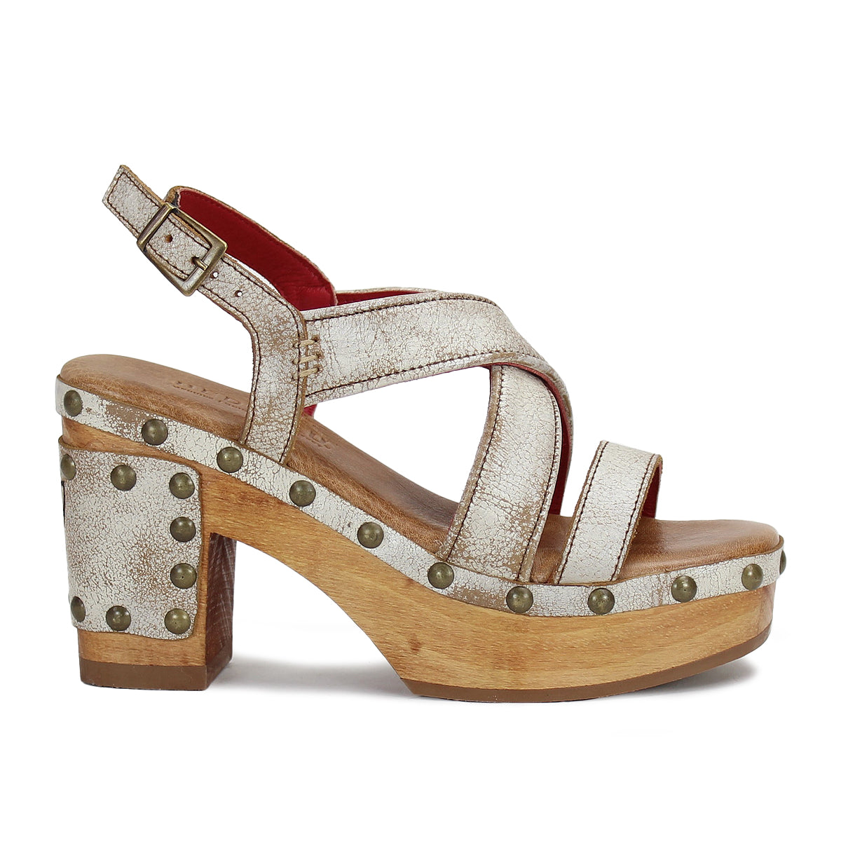 The Mediation by Bed|Stü is a chunky-heeled slingback sandal featuring wide metallic leather straps, a wooden sole accented with brass studs, a cushioned insole for extra comfort, and an adjustable ankle buckle.