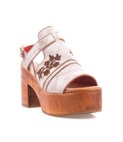 The Melodramatic sandal by Bed|Stü features a chunky wooden platform heel, a cream-colored upper crafted from leather with embroidered floral designs, an open toe, and an adjustable ankle strap with buckle.