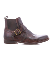 The Bed|Stü Michelangelo is a brown leather ankle boot featuring a side buckle accent, low heel, and pull tab at the back, with a durable rubber outsole, shown in a left side profile on a white background.