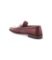 The Bed|Stü Moat, a single handcrafted loafer in rich brown leather, is displayed at an angle on a white background, highlighting the shoe’s side and back details.