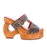 The "Mutable" by Bed|Stü is a wooden platform sandal featuring a curved, vintage-inspired wooden heel, a textured brown leather strap with a decorative buckle, and metallic rivet accents.