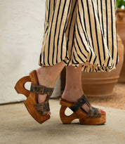 Wearing the Bed|Stü Mutable chunky wooden platform sandals, featuring cut-out heels and a decorative buckle, this look pairs perfectly with a beige and black striped skirt for a subtly vintage-inspired style.