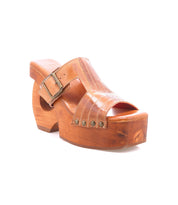 The Bed|Stü Mutable sandal features a brown wooden platform heel, vintage-inspired design, leather upper, metal stud accents, and a large decorative buckle, shown against a white background.