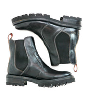 The Bed|Stü Nandi III is a pair of black leather Chelsea boots featuring dual side gores, elastic panels, pull tabs, and lug soles, displayed from the side and bottom on a white background—an effortlessly timeless boot.