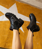 A person’s legs held up in the air wearing black leather Bed|Stü Nandi III Chelsea boots with thick lugged rubber soles for everyday function.