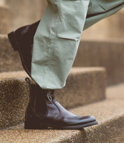 A person wearing light green pants and a pair of Bed|Stü Nando dark brown hand-worked leather Chelsea boots stands on stone steps.