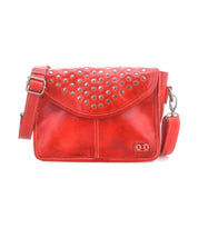 The Bed|Stü Occurrence is a red leather compact crossbody featuring metal studs on the flap, an adjustable strap, and a small stitched logo at the front bottom right corner. This studded bag from Bed|Stü effortlessly blends bold style with everyday practicality.
