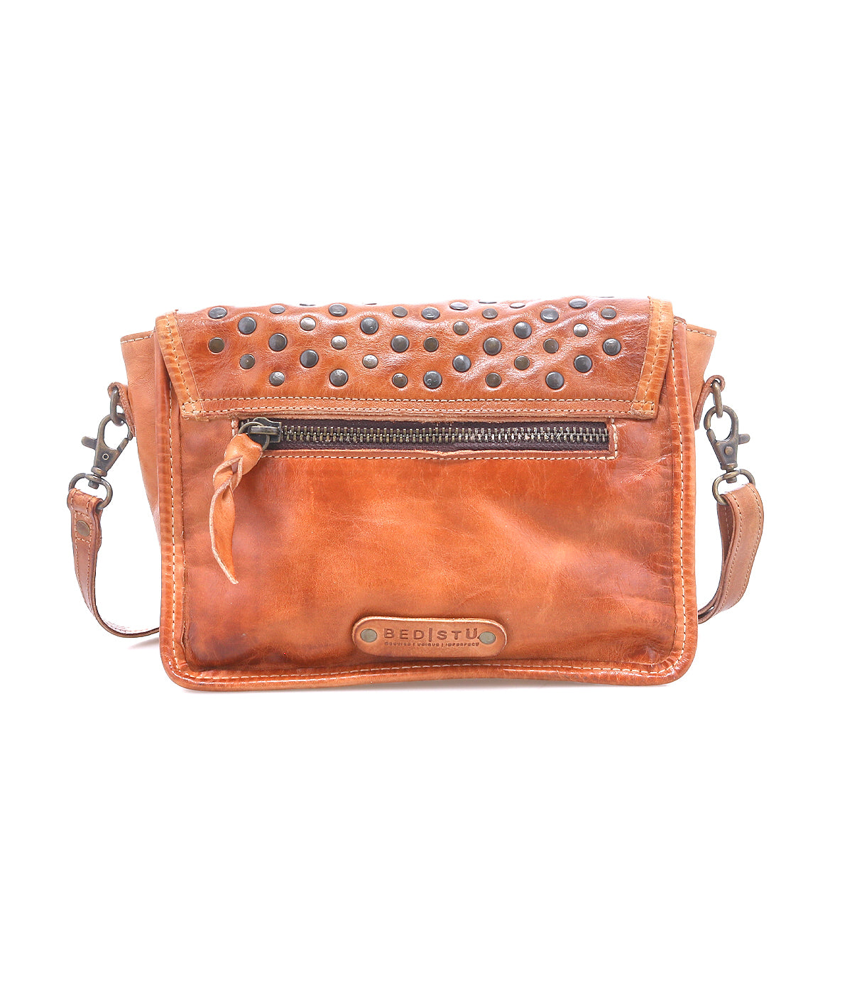 Bed|Stü Occurrence is a brown leather compact crossbody bag featuring metal studs on the flap, a front zipper pocket, and a BED|STU logo patch at the bottom center.