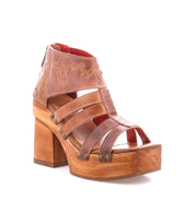 The Orphyx sandal by Bed|Stü is a brown leather strappy design featuring layered leather straps, metal rivet accents, and an open-toe silhouette atop a chunky sculpted wood platform heel, shown against a white background.